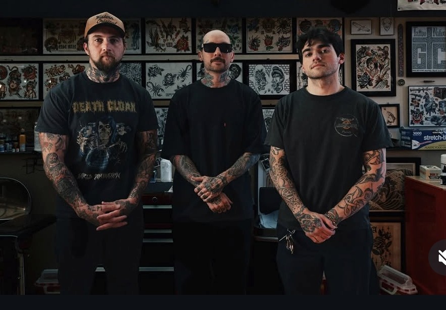 Three tattooers standing in front of a wall of flash in their shop
