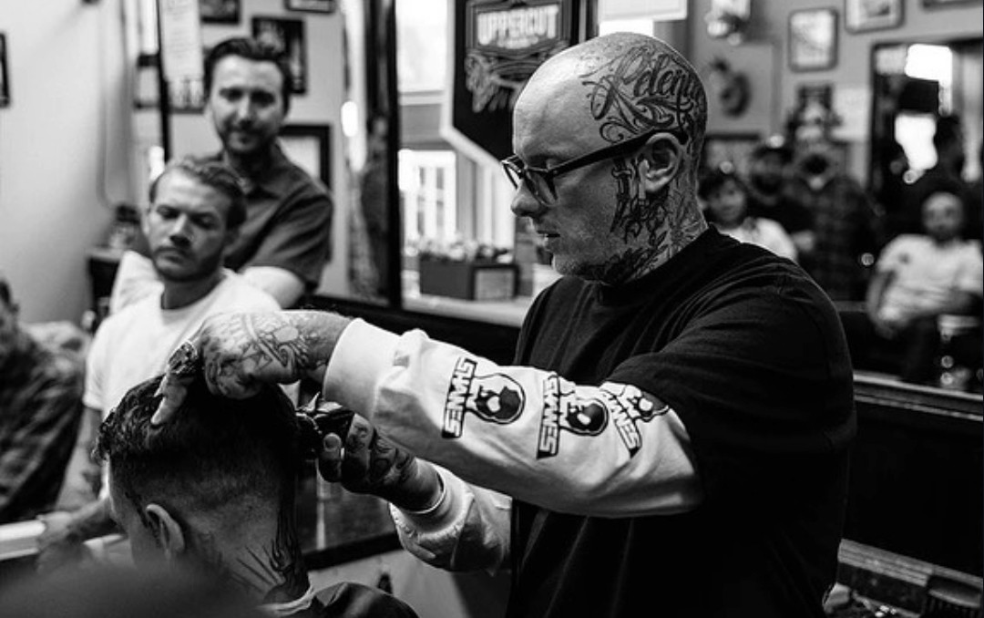 Tattooed barber cutting hair in a full shop